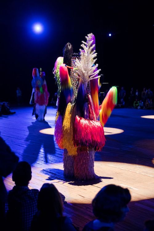 A Nick Cave soundsuit that includes colors of magenta, lime green, bright yellow and the suit has silver tinsel poking out.